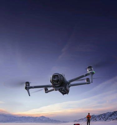 Drone flying over a snowy landscape with a person in the background, sold by a DJI Authorized Retailer.
