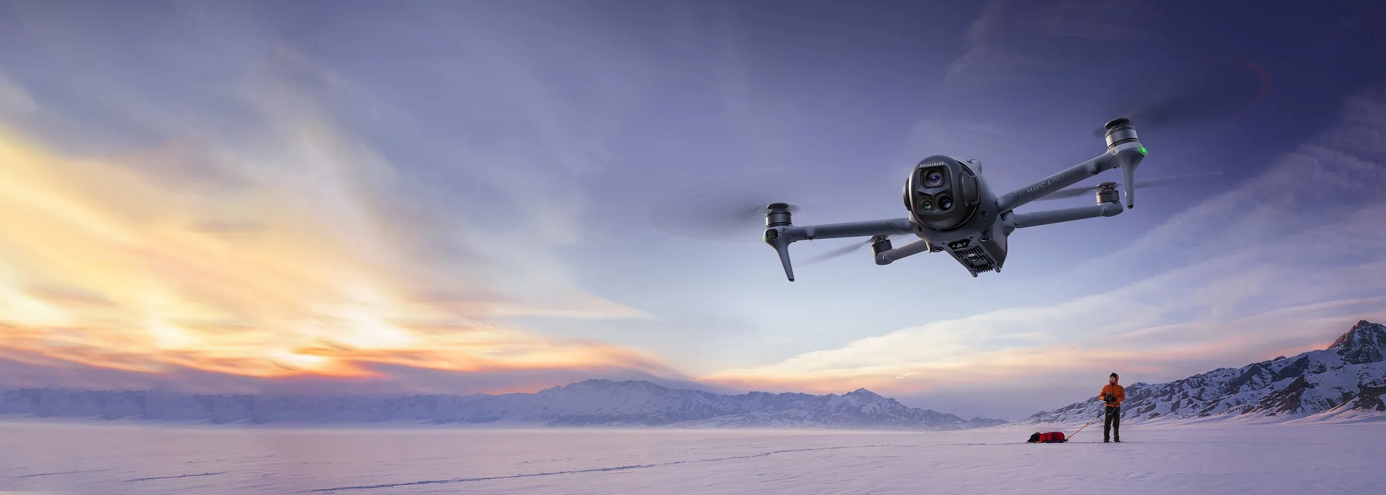 Drone flying over a snowy landscape with a person in the distance at sunset. Sold by an Authorized DJI Retailer.