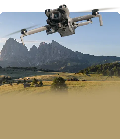 Drone flying over a scenic landscape with mountains and fields. Sold by a DJI authorized retailer.