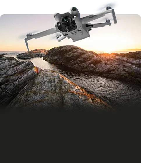 Drone flying over rocky terrain with a sunset in the background. Sold by a DJI authorized retailer.